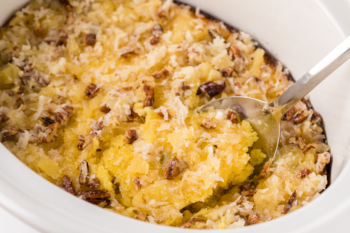 close up of pineapple spoon cake in a white slow cooker with a spoon.