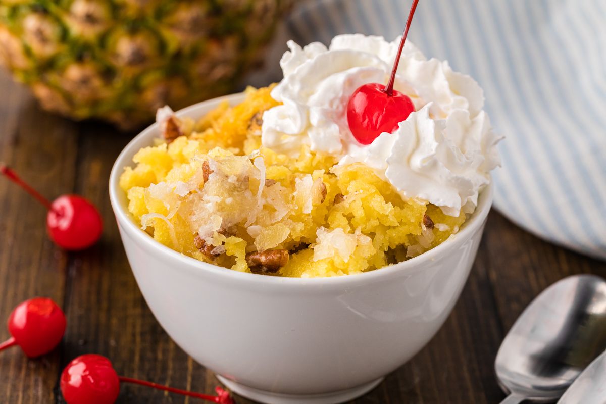 bowl of pineapple spoon cake with whipped cream and a cherry.