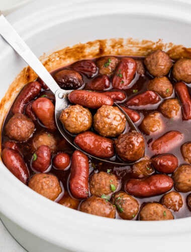 close up of meatballs and little smokies in a white slow cooker.