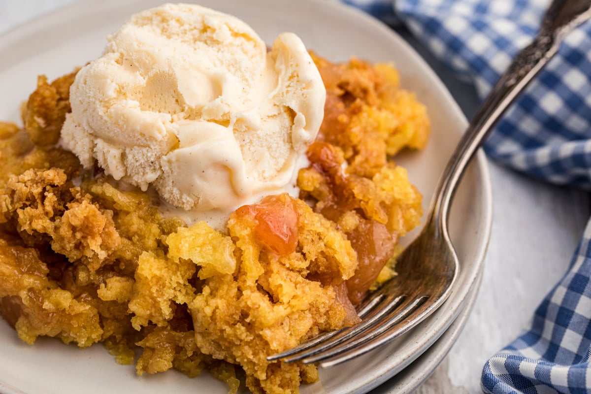 close up of apple dump cake with ice cream with a fork.