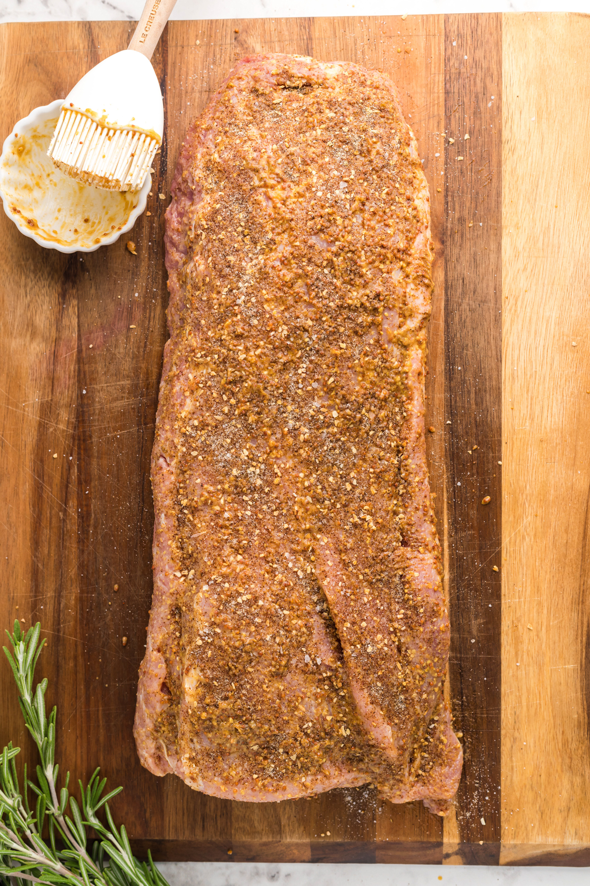 overhead of seasoned raw pork loin on a wooden board.