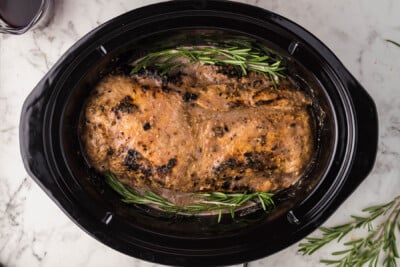 pork loin in a slow cooker before cooking with sauce and rosemary springs added.