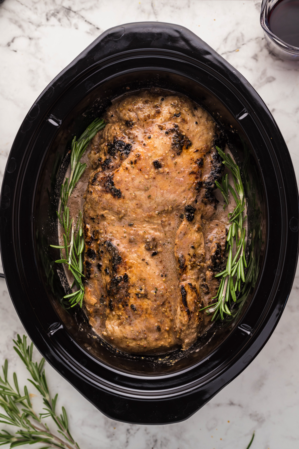 pork loin in a slow cooker before cooking with sauce and rosemary springs added.