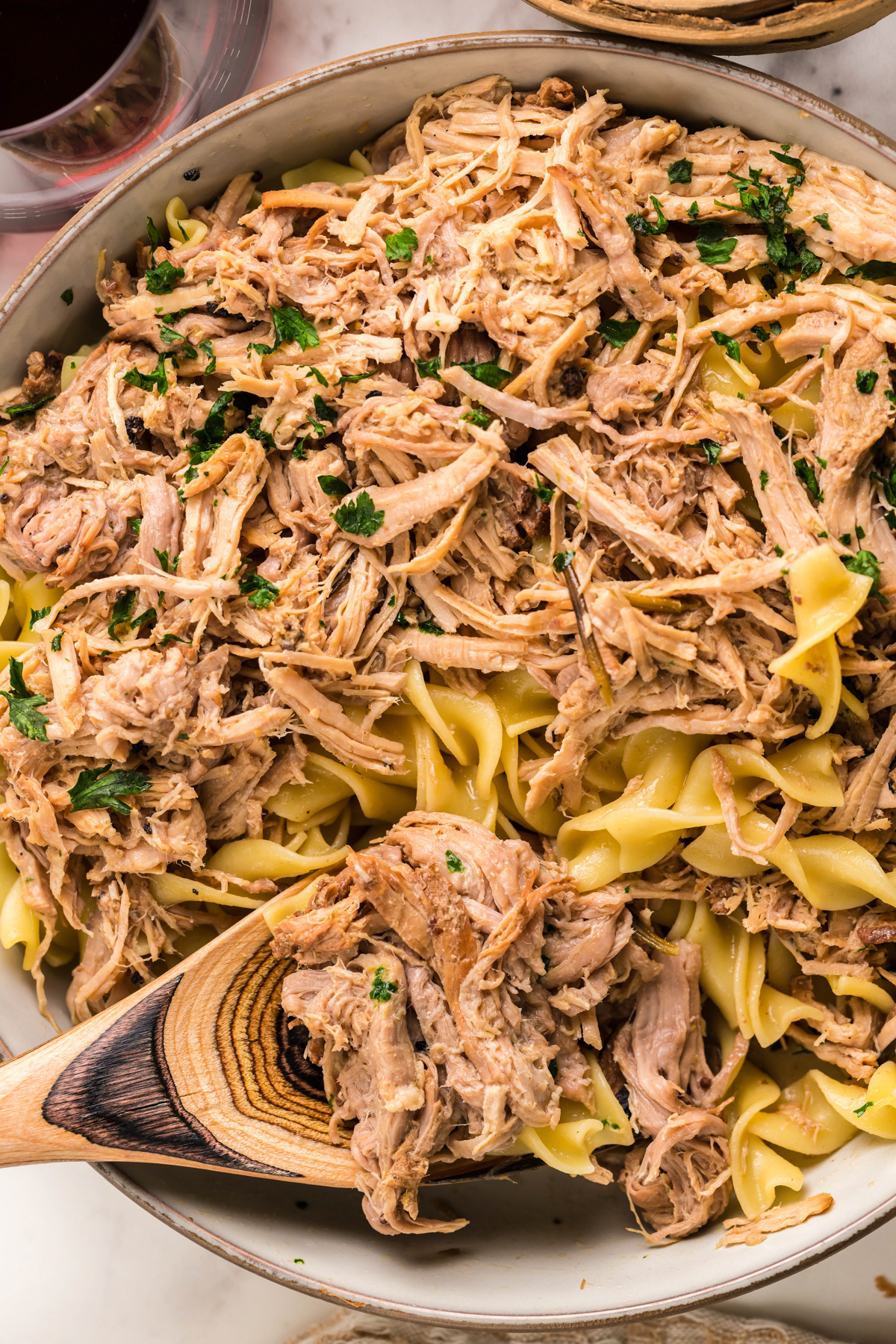 close-up of slow cooker pulled pork pasta in a serving bowl with a spoon in it.