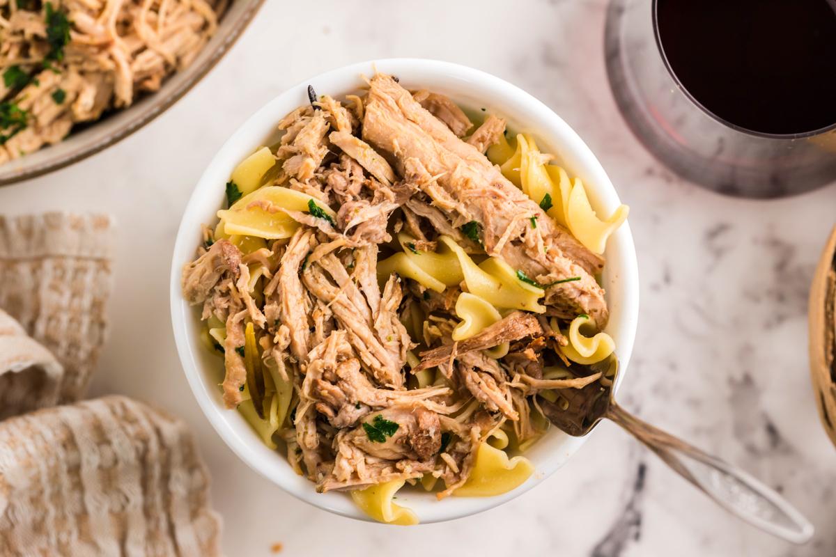 overhead of serving of slow cooker pulled pork pasta in a white bowl with a fork.