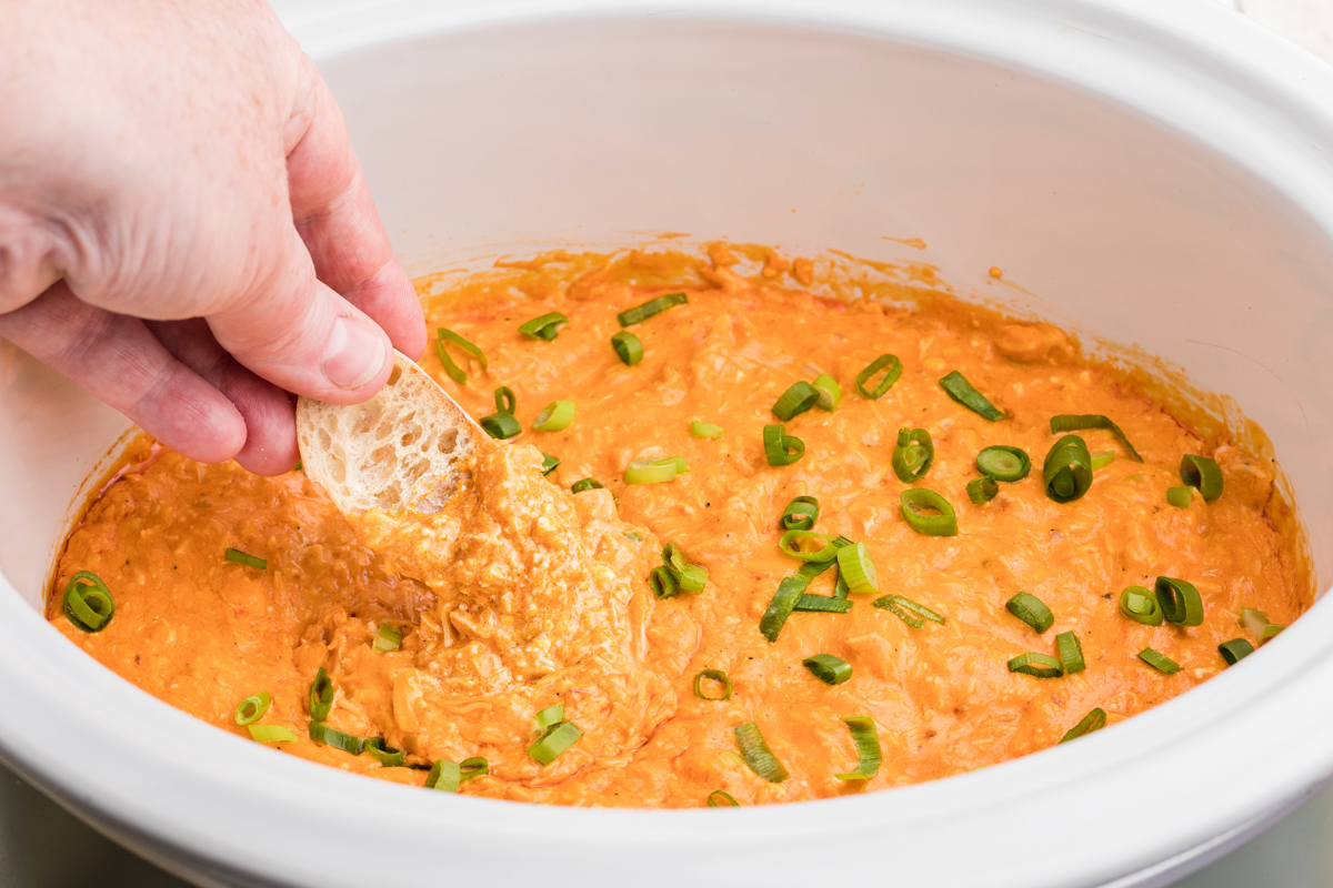 buffalo dip with a piece of bread being dipped in it.
