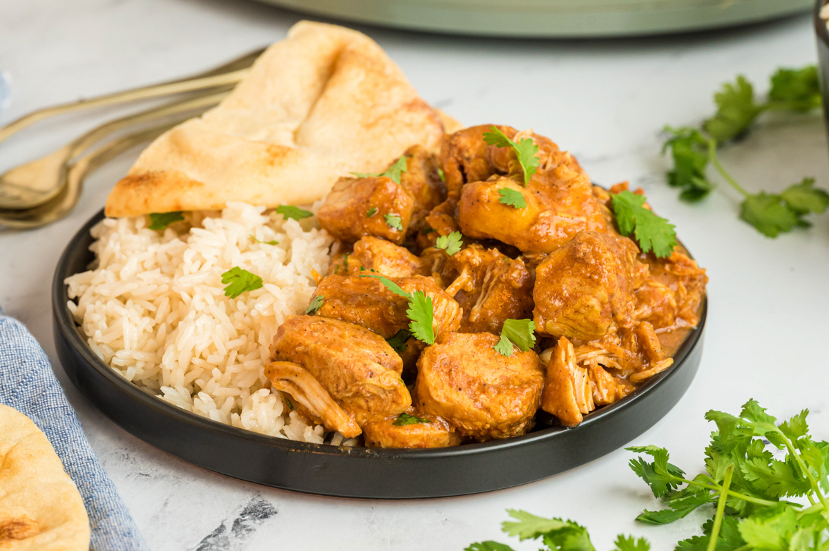 plate of butter chicken with rice and naan.