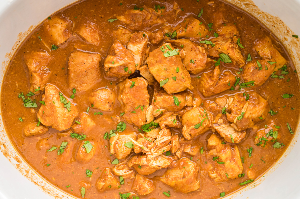 butter chicken cubes in a slow cooker with cilantro.