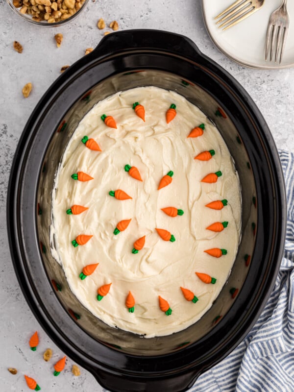 carrot cake with icing and carrots on top in a slow cooker.
