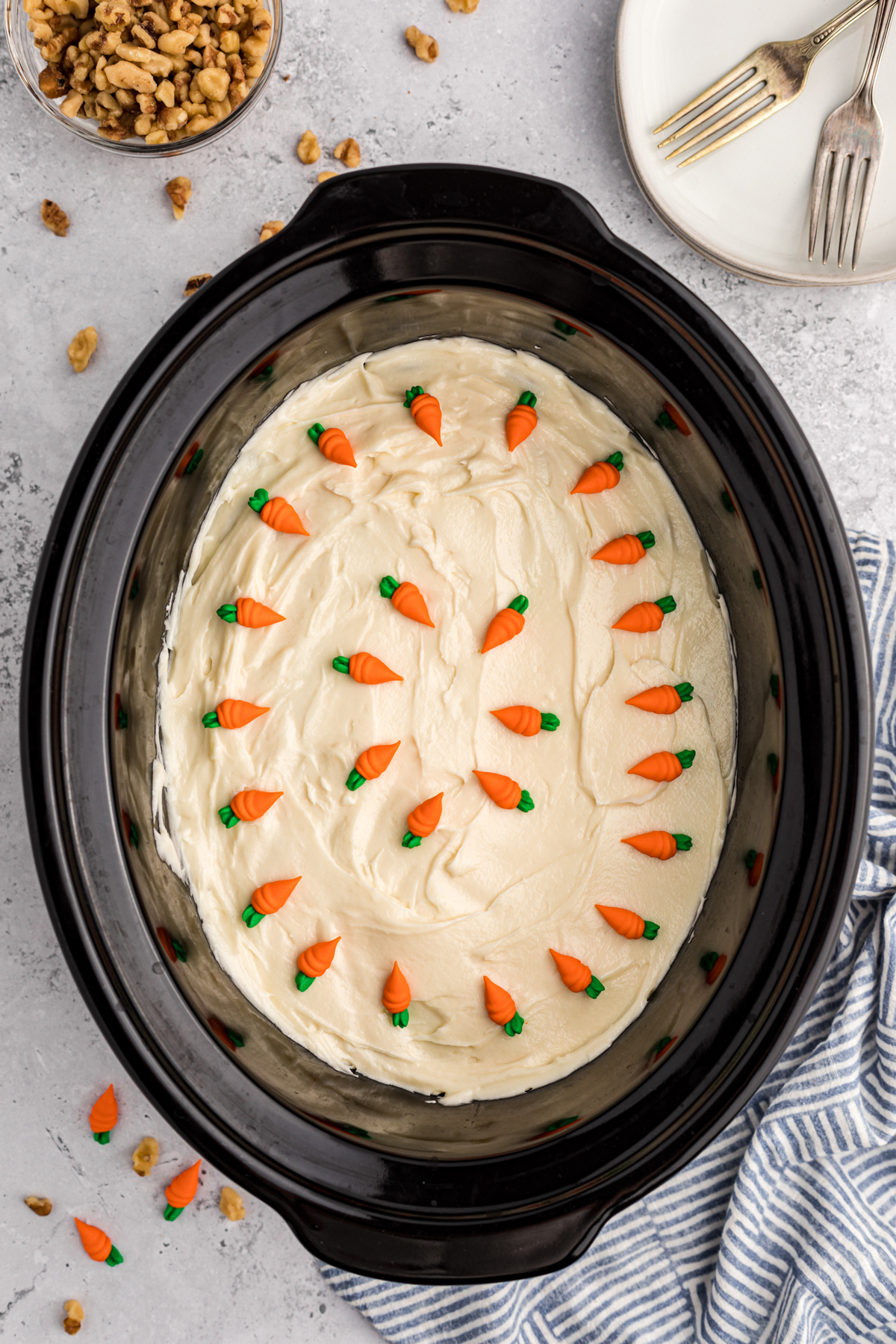 carrot cake with icing and carrots on top in a slow cooker.