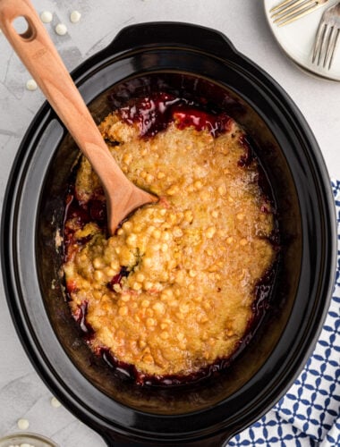 Cherry dump cake in the slow cooker with a wooden spoon in it.