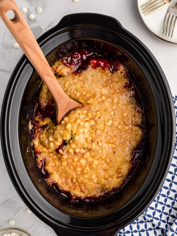 Cherry dump cake in the slow cooker with a wooden spoon in it.