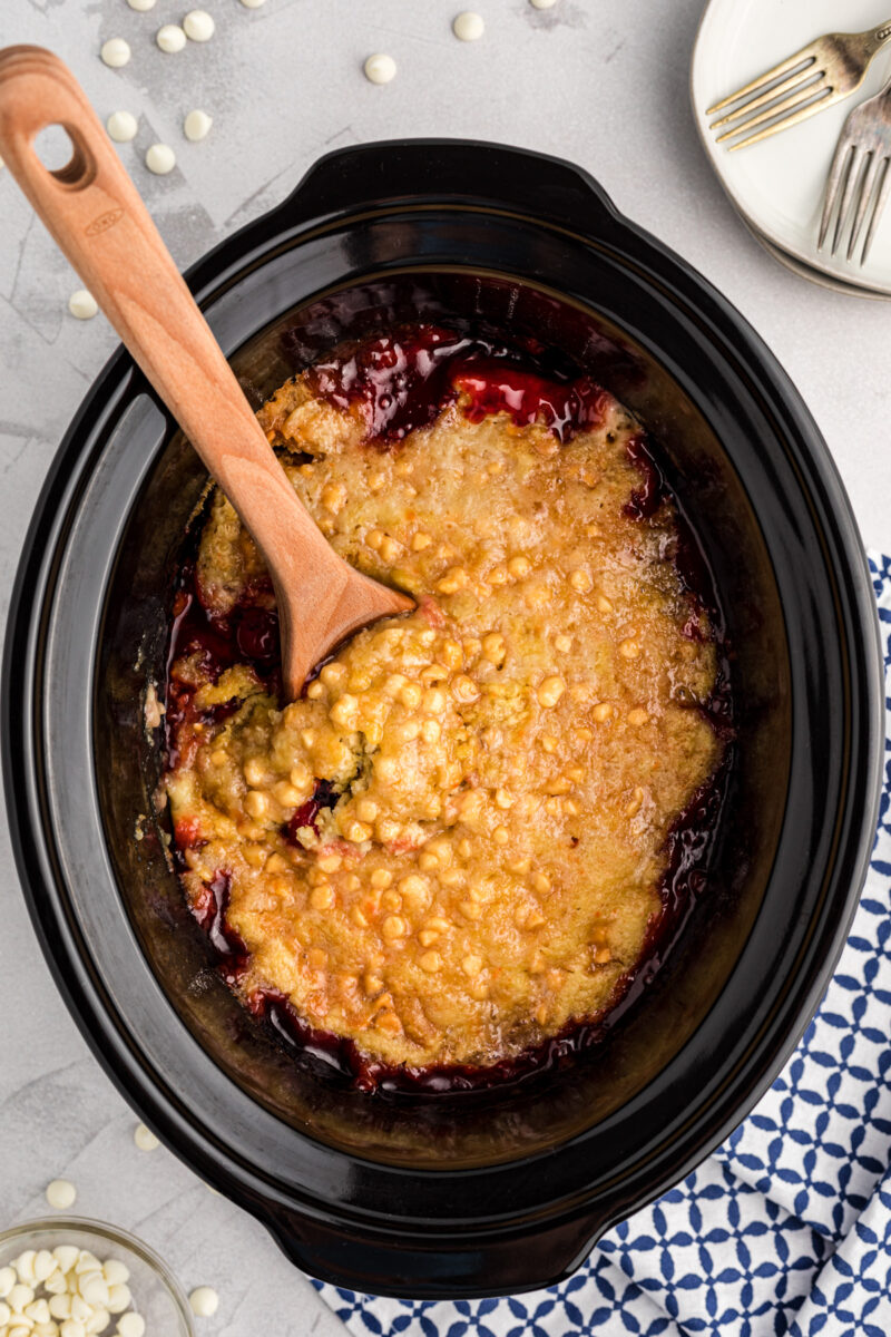 Cherry dump cake in the slow cooker with a wooden spoon in it.