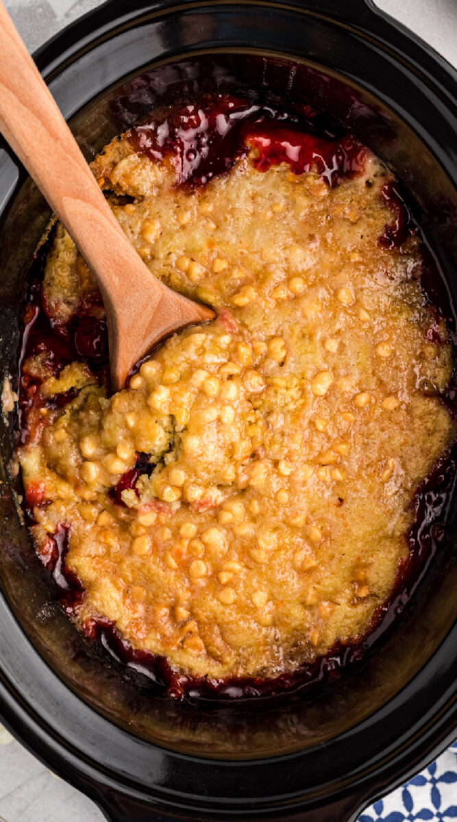 close up of cherry dump cake in a slow cooker with a spoon.