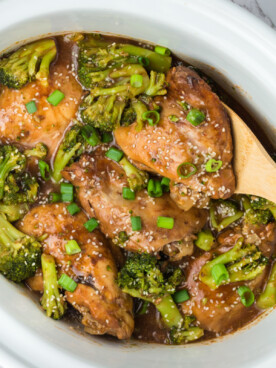 chicken and broccoli in a slow cooker with a wooden spoon in it.