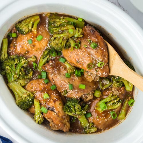 chicken and broccoli in a slow cooker with a wooden spoon in it.