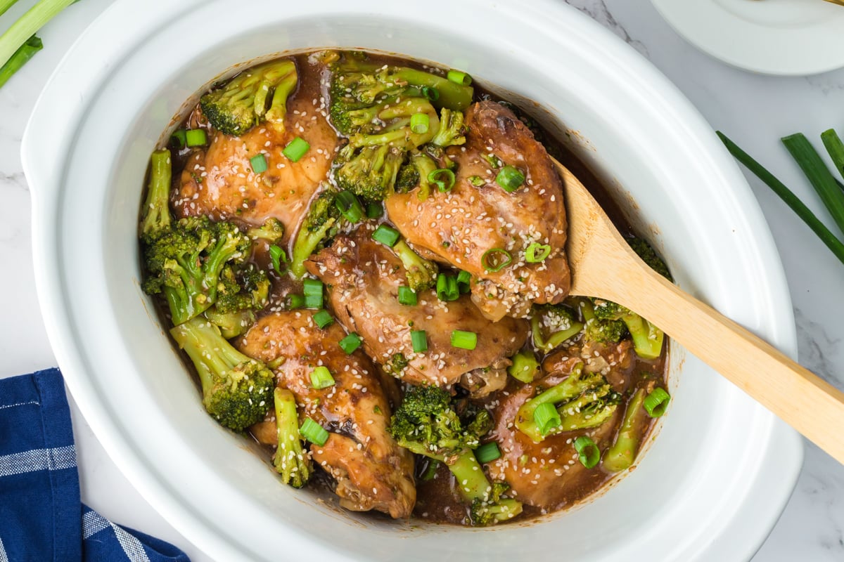 chicken and broccoli in a slow cooker with a wooden spoon in it.