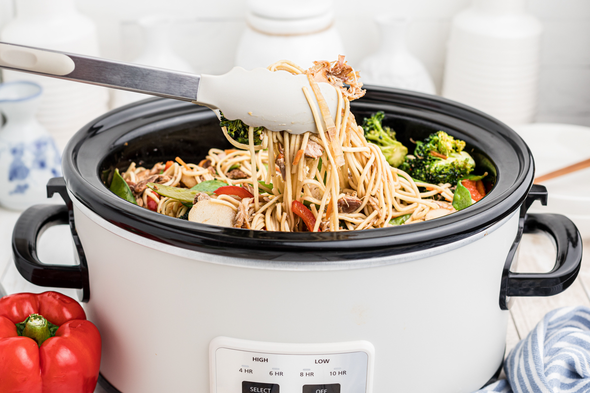 chow mein coming out of slow cooker on tongs.