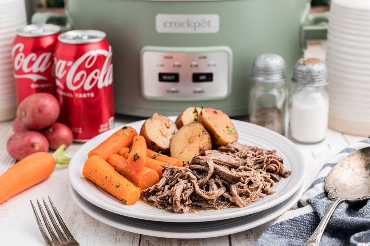 pot roast and vegetables on a plate with coke cans in the background.