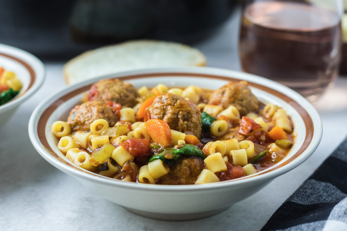 meatball soup with pasta and spinach in a bowl.