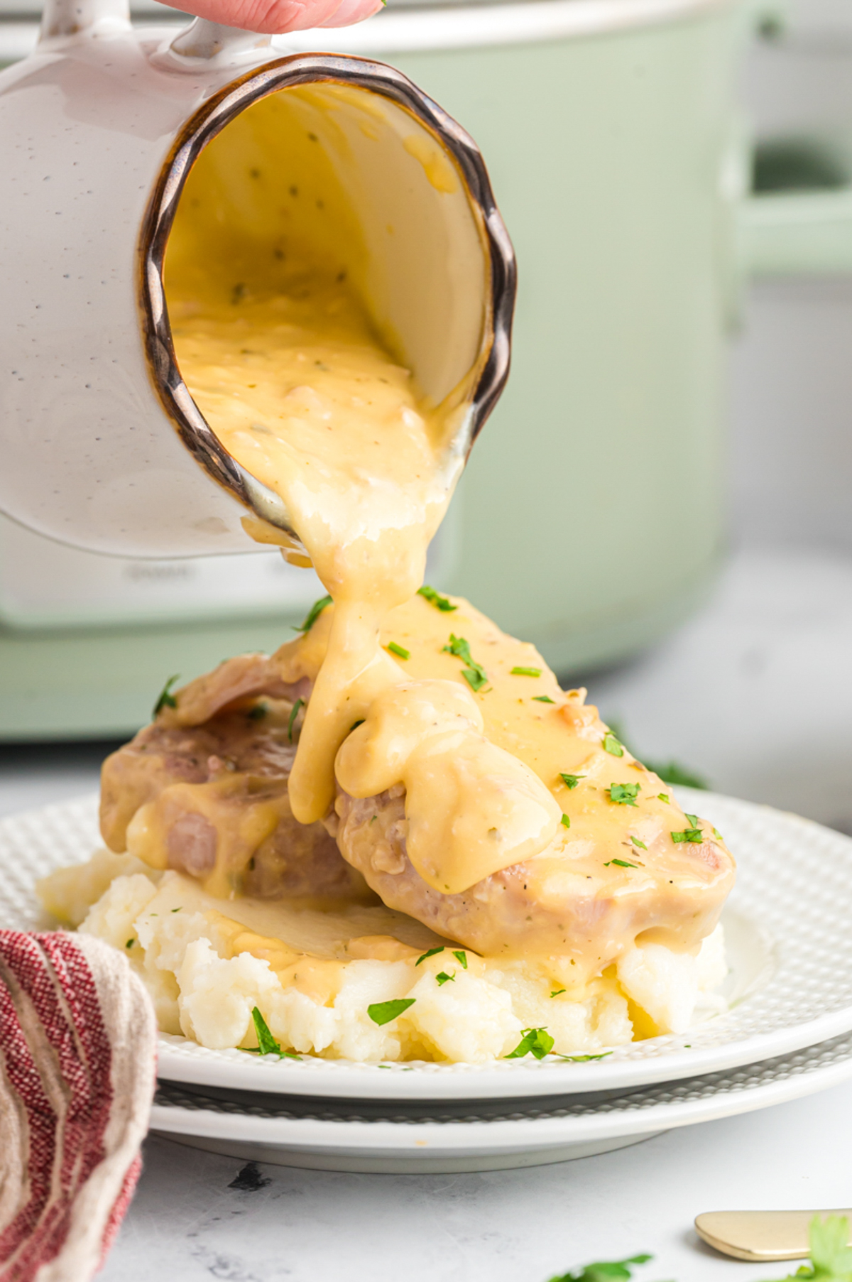plate of ranch pork chops on a plate of mashed potatoes with gravy being poured over.