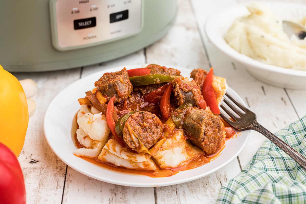 Plate of sausage and peppers over mashed potatoes.