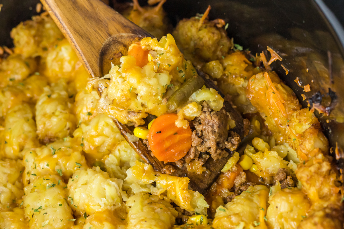 close up of shepherd's pie tater tot casserole on a wooden spoon in a crockpot.