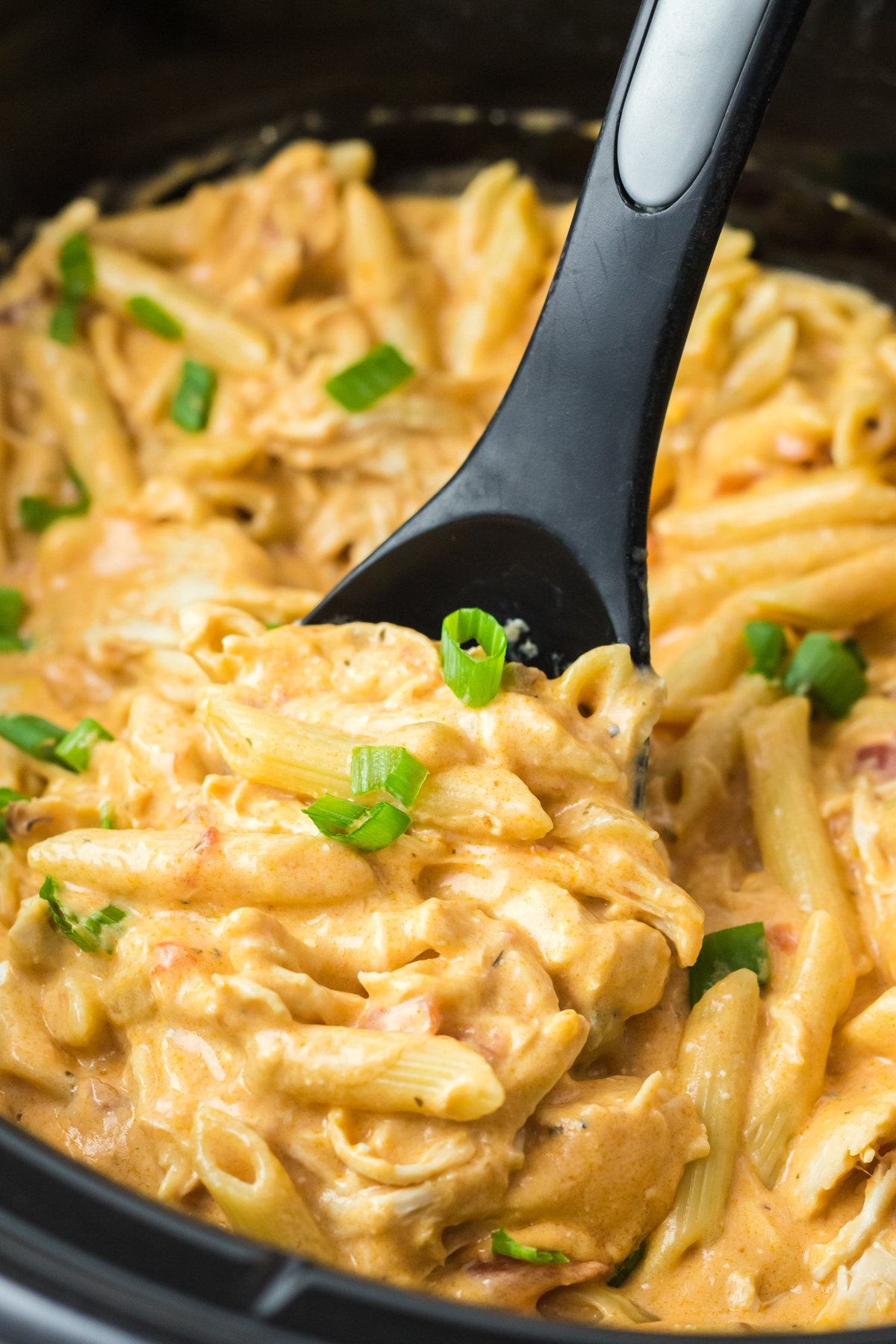 close up of buffalo chicken pasta in a slow cooker with a spoon in it.