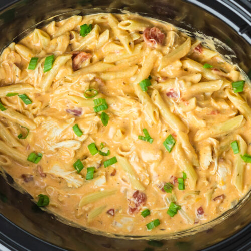 buffalo chicken pasta in a crockpot with green onions on top.