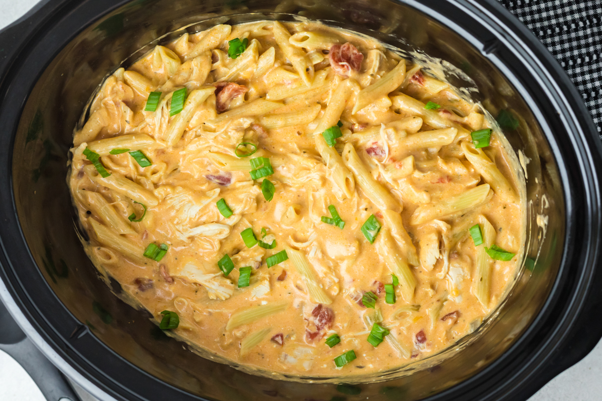 buffalo chicken pasta in a crockpot with green onions on top.