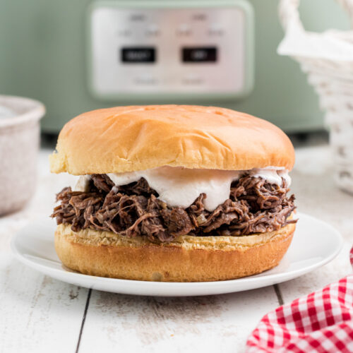 Shredded beef sandwich on a plate with horseradish sauce on it.
