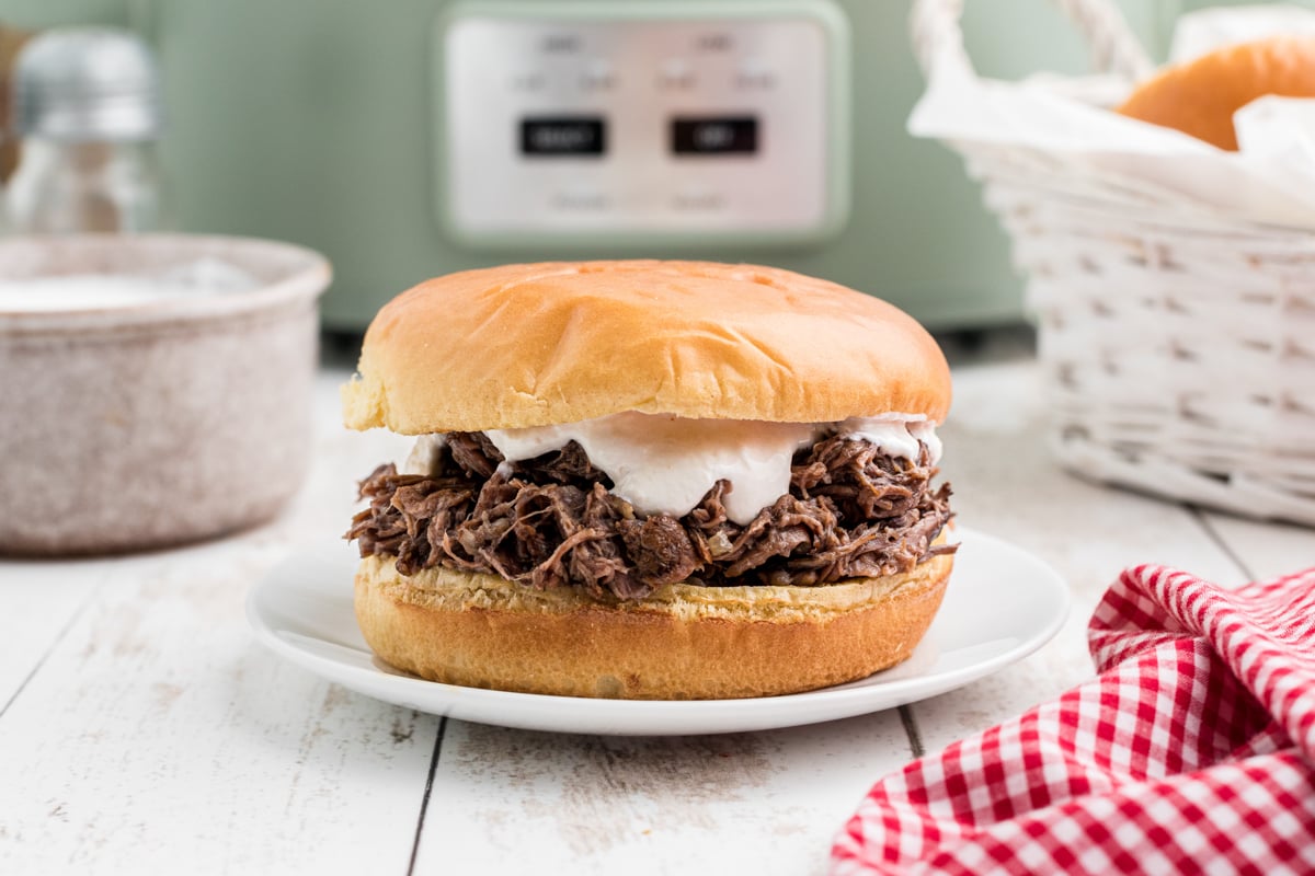 Shredded beef sandwich on a plate with horseradish sauce on it.