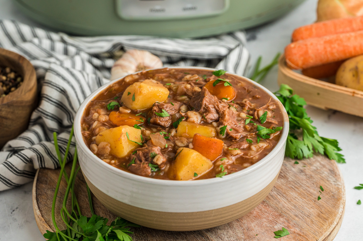 bowl of beef barley soup with crockpot in back ground.