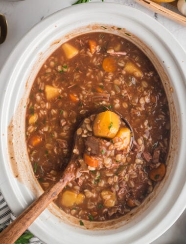beef barley soup on a wooden spoon coming from a slow cooker.