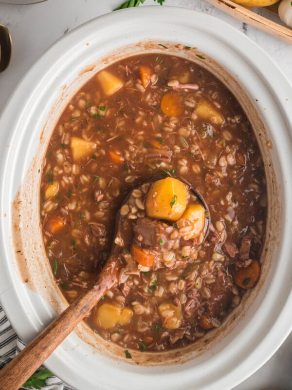 beef barley soup on a wooden spoon coming from a slow cooker.