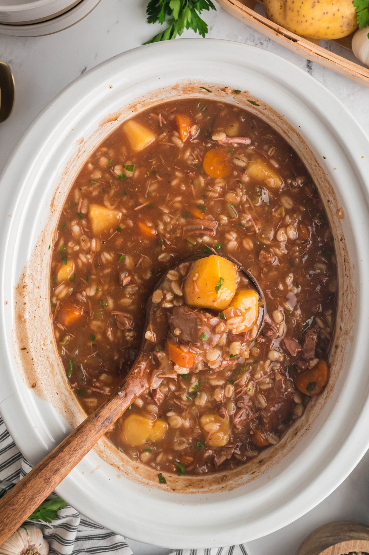 beef barley soup on a wooden spoon coming from a slow cooker.