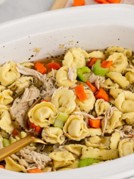 chicken tortellini in a white slow cooker with a wooden spoon in it.
