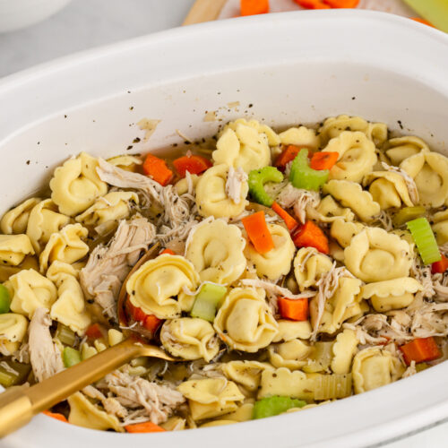 chicken tortellini in a white slow cooker with a wooden spoon in it.