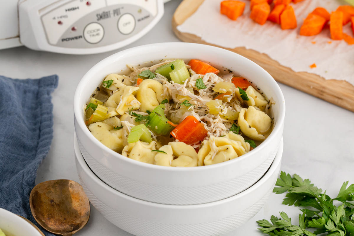 bowl of chicken tortellini soup with slow cooker in the background.