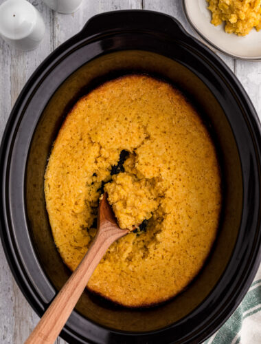 crock pot full of corn casserole with wooden spoon in it.