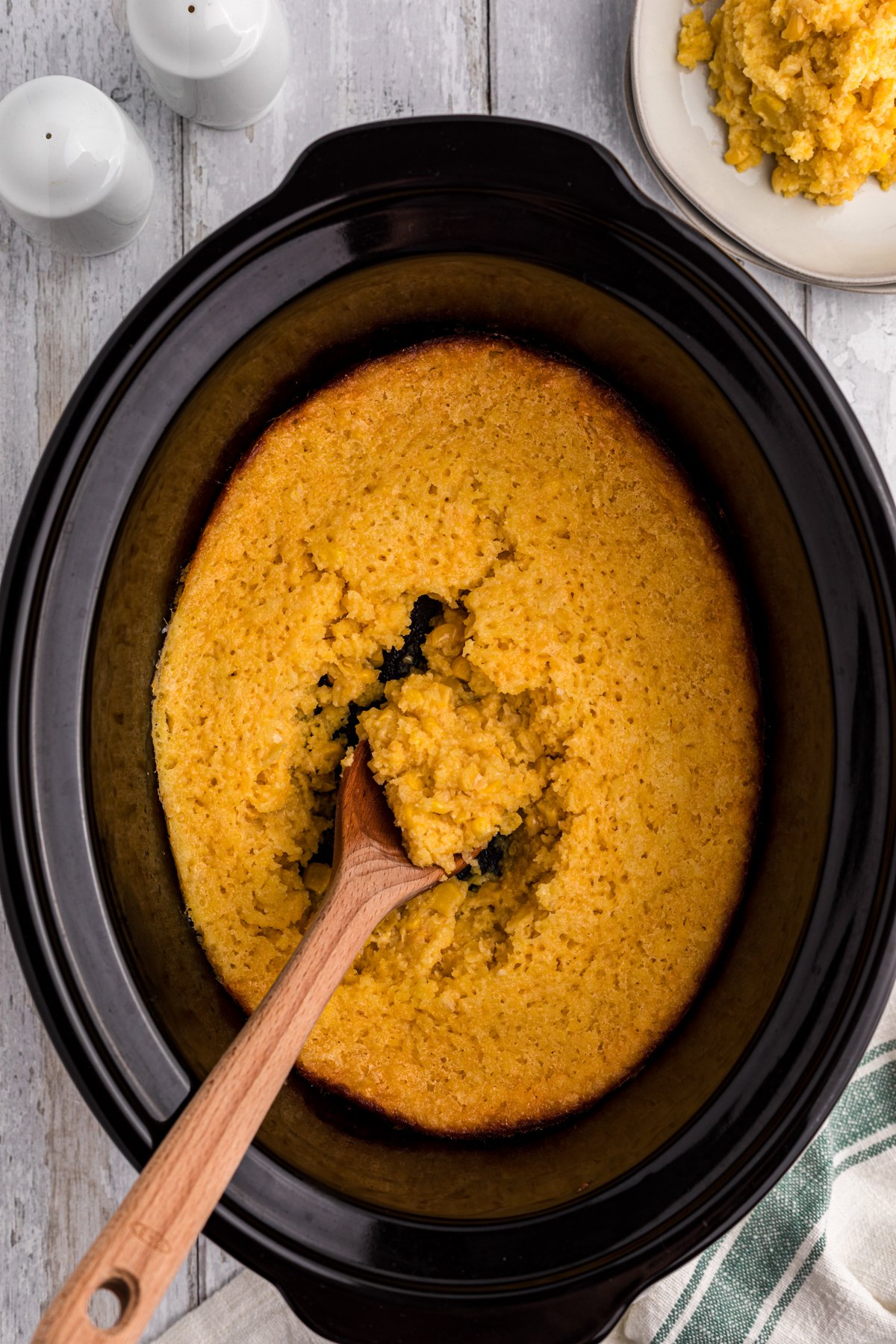 crock pot full of corn casserole with wooden spoon in it.