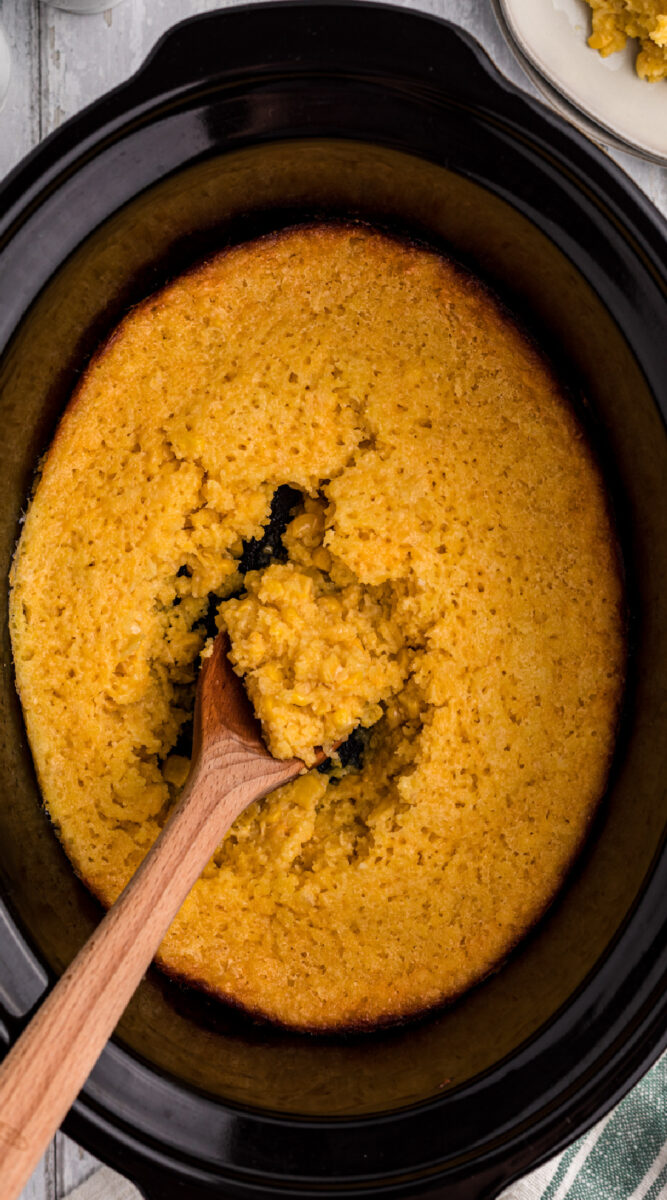 long image of corn casserole with spoon in it.