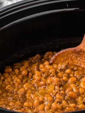 Pot of baked cowboy beans with a wooden spoon in them.