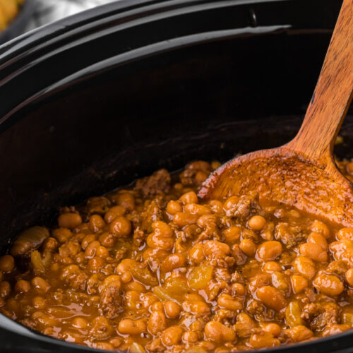 Pot of baked cowboy beans with a wooden spoon in them.