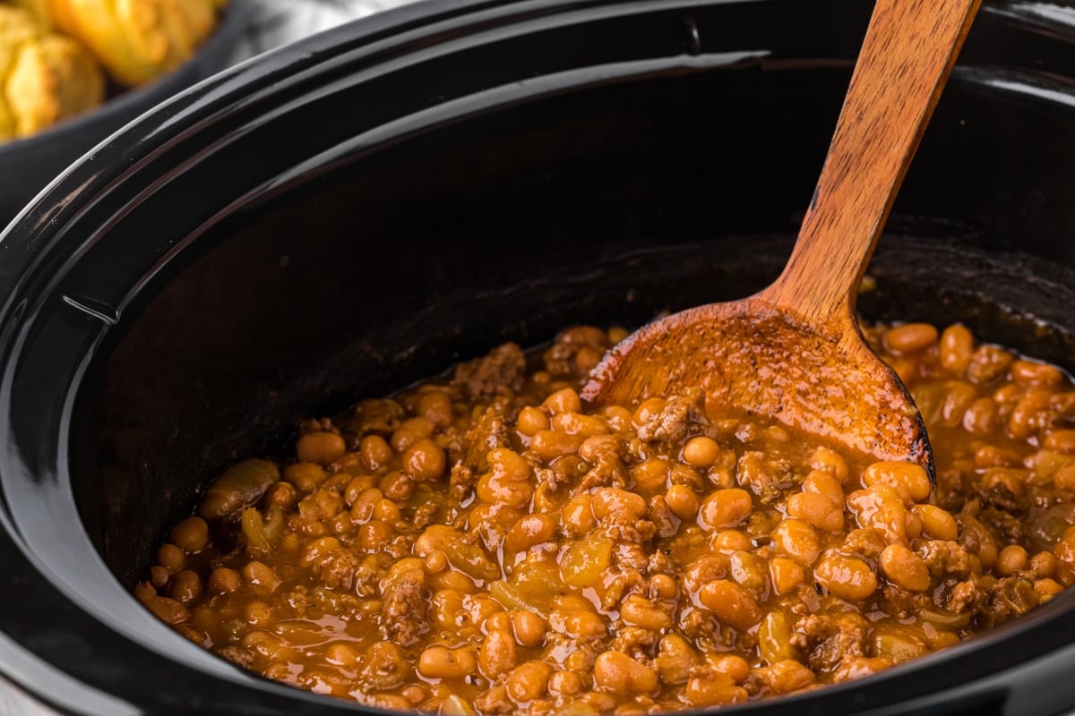 Pot of baked cowboy beans with a wooden spoon in them.