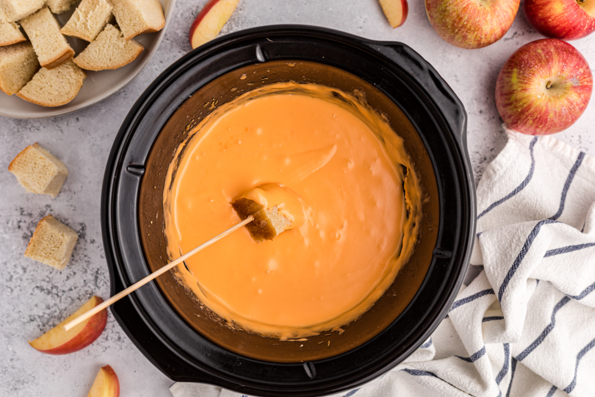 cheese fondue in a slow cooker with a piece of bread being dipped in.