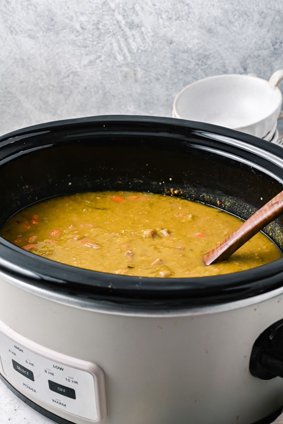 Split pea soup in a slow cooker with a wooden spoon in it.