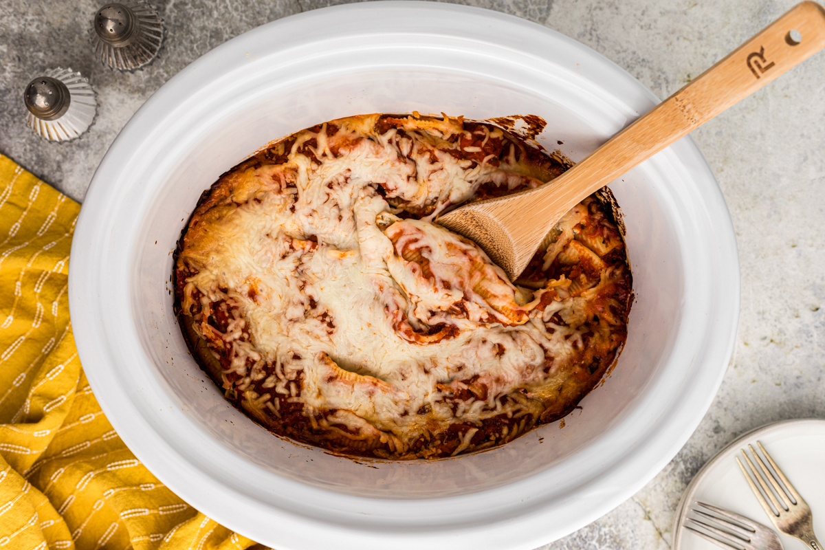 Stuffed shells in a slow cooker with a wooden spoon in it.