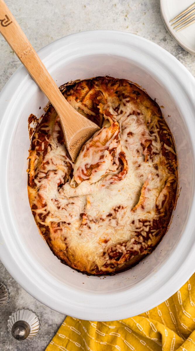 long image of stuffed shells in a slow cooker with spoon in it.