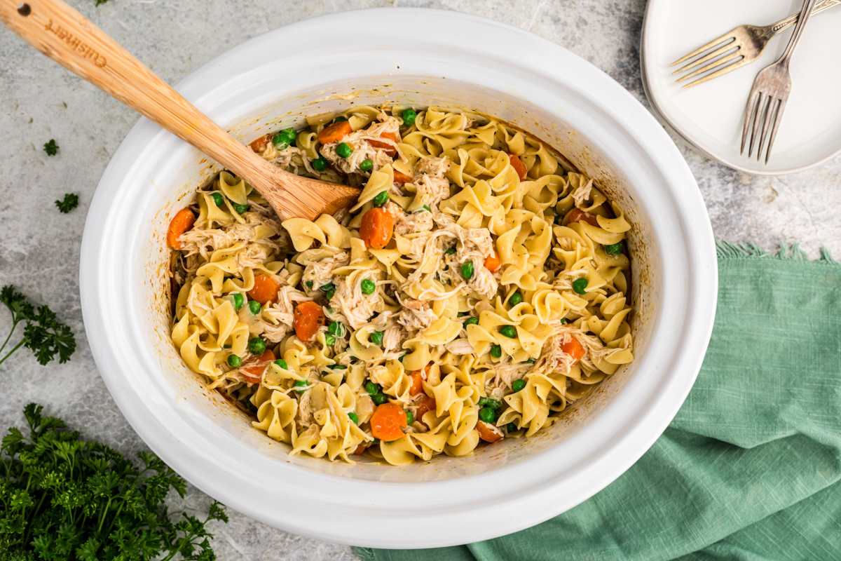 noodles and chicken with peas and carrots in a slow cooker.